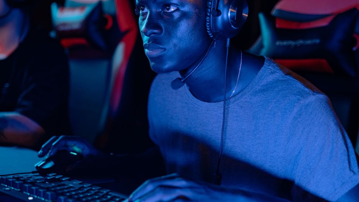 Photo d'illustration&nbsp;: un joueur concentré devant son écran la nuit, casque audio sur la tête, dans une pièce éclairée en bleu et rouge.