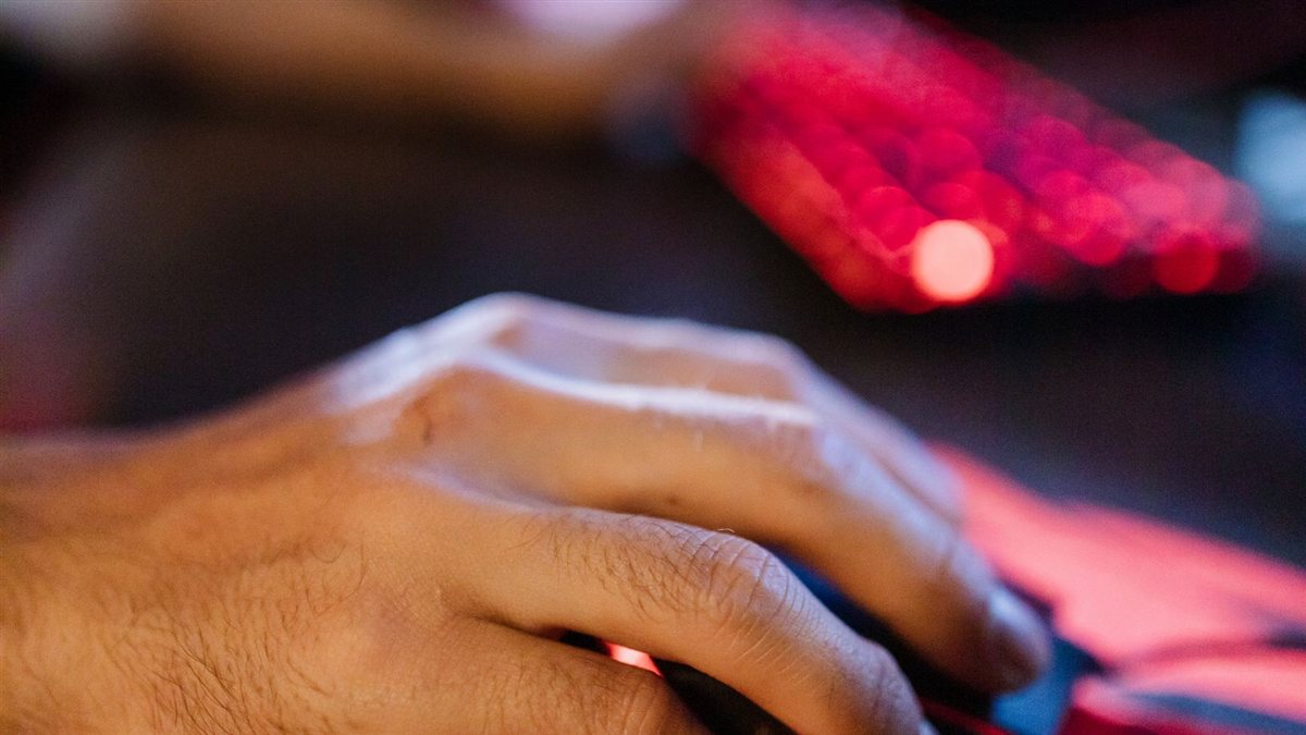 Main d'un joueur sur une souris gaming posée sur un tapis rétroéclairé : la mémoire musculaire est construite sur la distance parcourue par la souris, pas sur le chiffre du menu