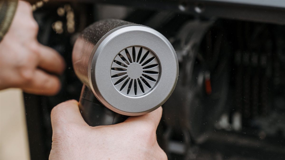 Personne dépoussiérant l'intérieur d'un PC fixe à l'aide d'une soufflette pour retirer la poussière accumulée sur les composants